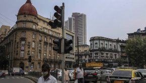 Pedestrians wearing protective masks walk past an out of service traffic signal as the Bombay Stock Exchange (BSE) building stands in the background in Mumbai on 12 October 2020