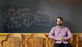 Man in front of a blackboard that has "Cas-13 detection" with star-like shapes underneath and pointing to "Microwell array"