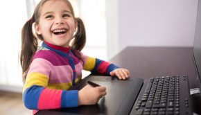 Little girl with pigtails smiling off camera while sitting in front of a computer