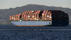 A large cargo ship on the ocean with a hill in the background