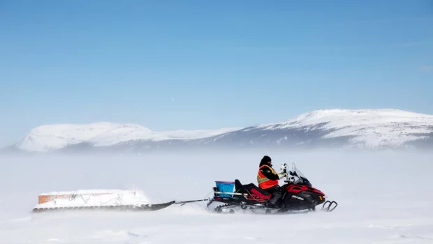 In a snowy environment, someone is pictured on a skidoo with a sleigh behind it.