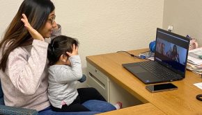 a mom and daughter sitting at an L-shaped desk doing a Zoom call on a laptop