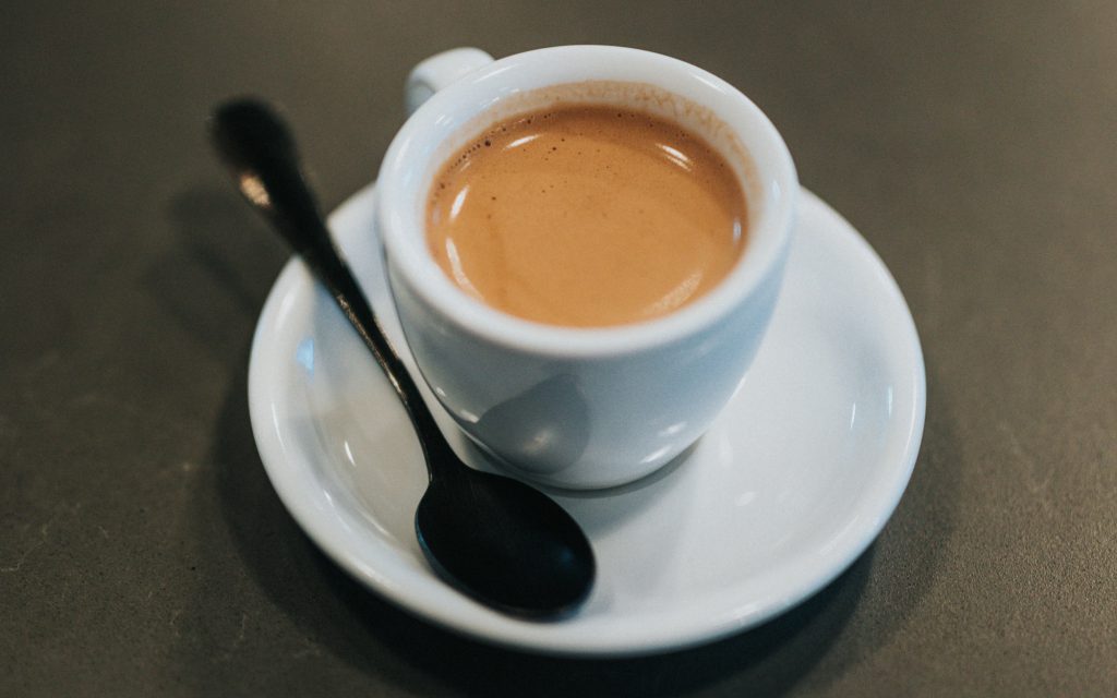 A single espresso served on a plate with a spoon