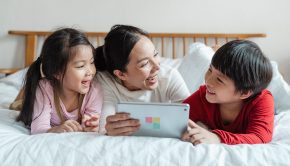 a happy family use a tablet lying on a bed