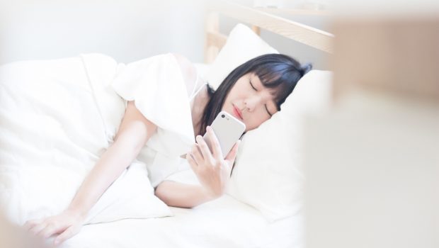 Woman lying in bed using her phone as she falls asleep