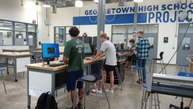 students in the drone program stand at their desks working on their laptops