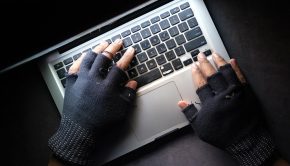 A hacker wearing gloves coding on a laptop