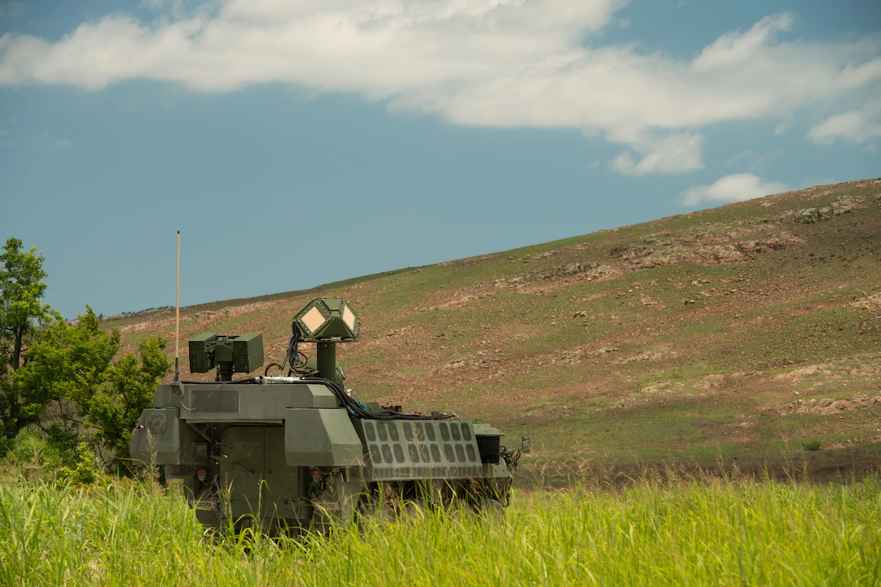 A military vehicle is positioned at the bottom of a hill. A cluster of instruments with reflective panels juts out of the top.
